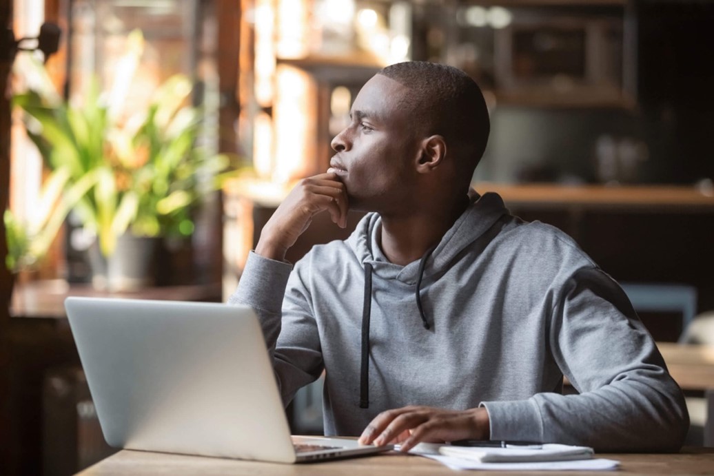 A young student sits at a laptop and looks out of the window.