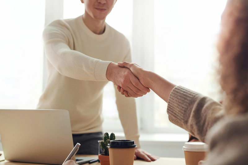 a man standing up behind a desk shaking the hand of a woman sitting