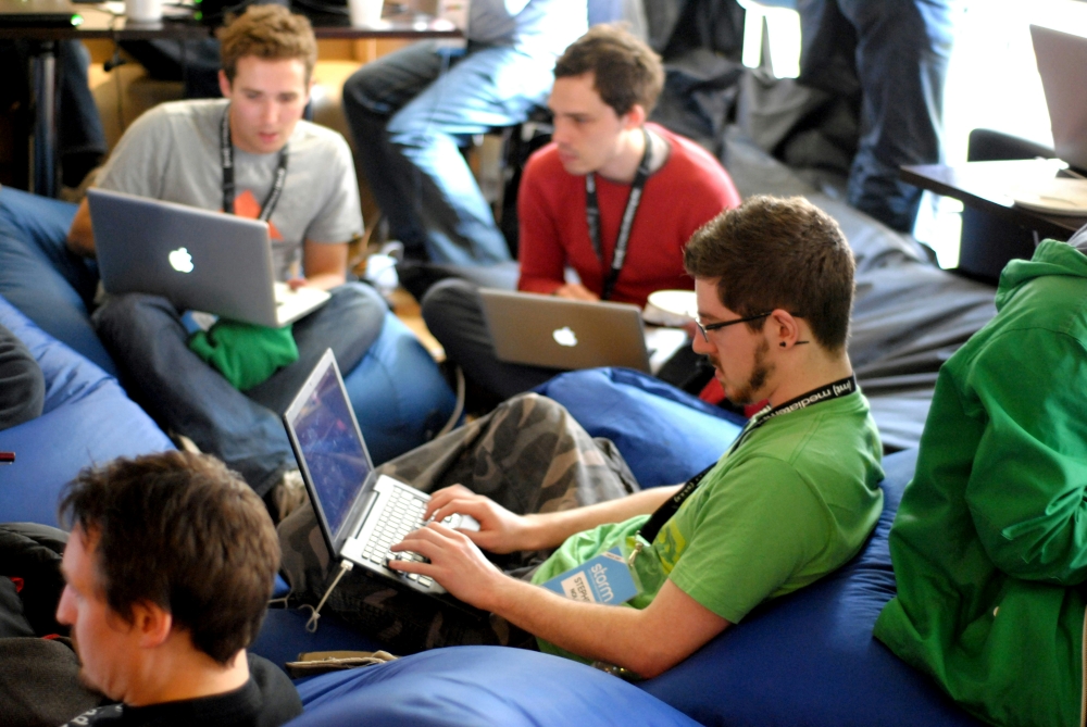 A group of young people sat on comfortable low chairs  on laptops.