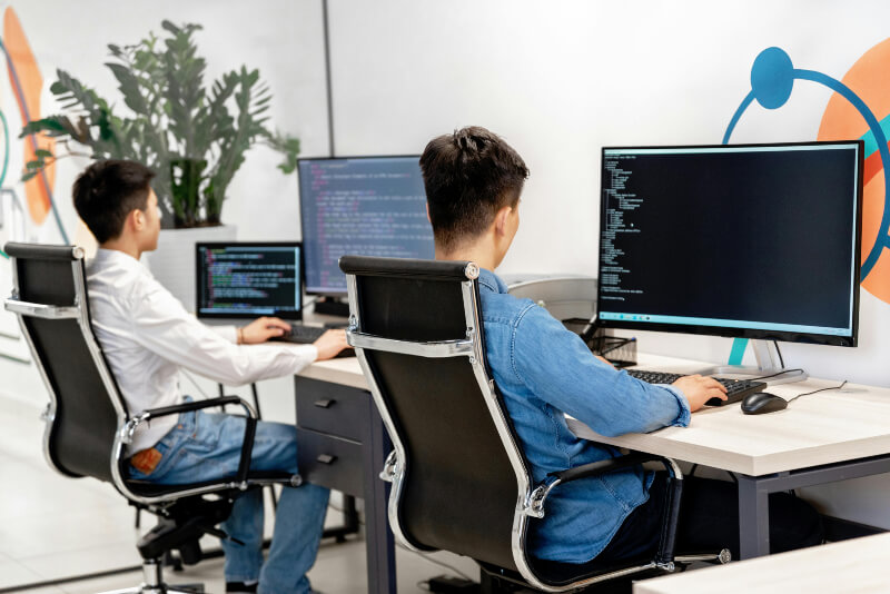 Two young people are sat at their desks, using computers.
