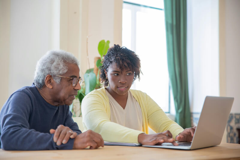 A younger woman sat next to an older man showing him how to use a computer