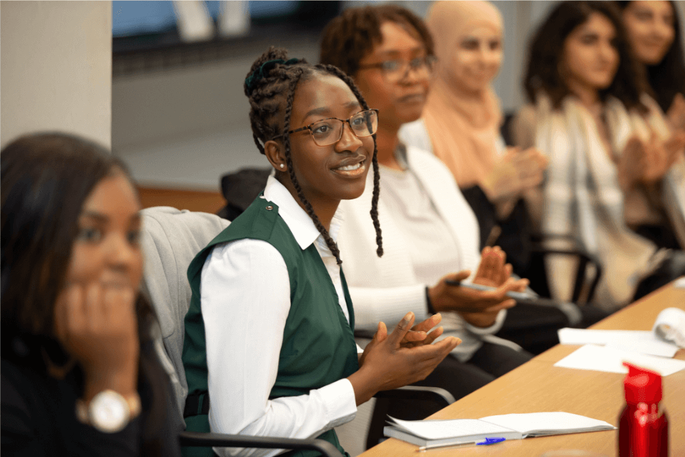 A group of women on an LTSB programme applaud while sat watching a talk.