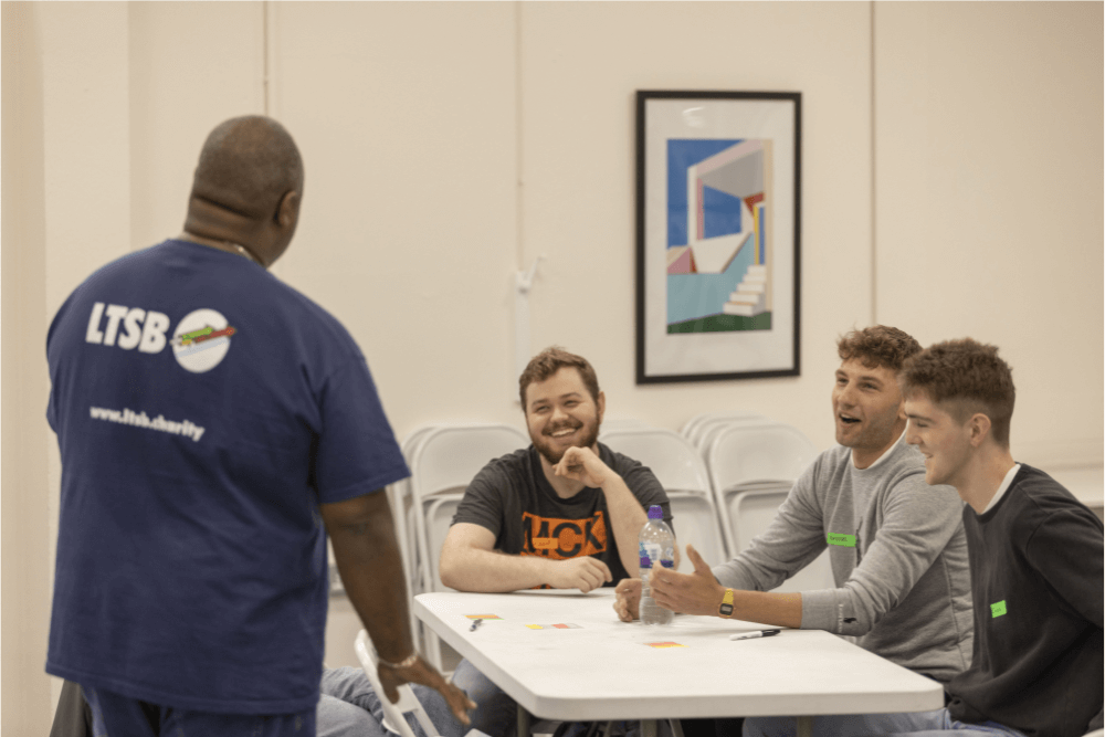 Three young men laugh while speaking to an LTSB programme worker.
